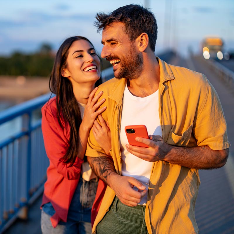 Laughing couple on a bridge with a phone at sunset